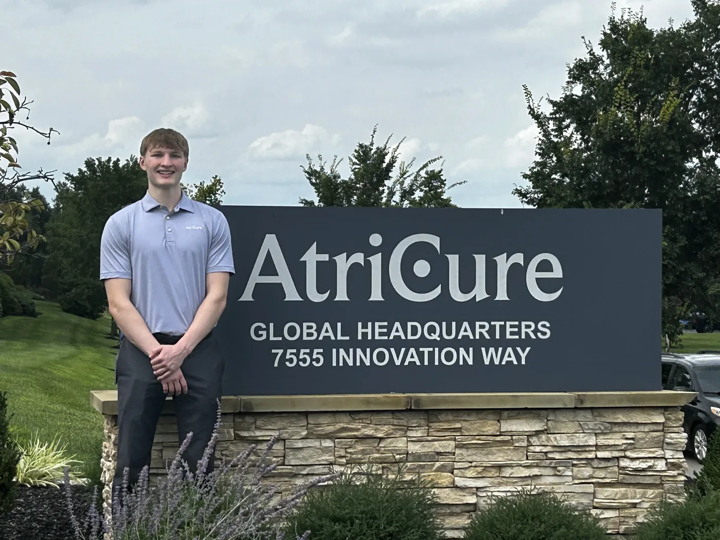 Aiden Knecht standing beside the AtriCure global headquarters sign in Mason, Ohio.